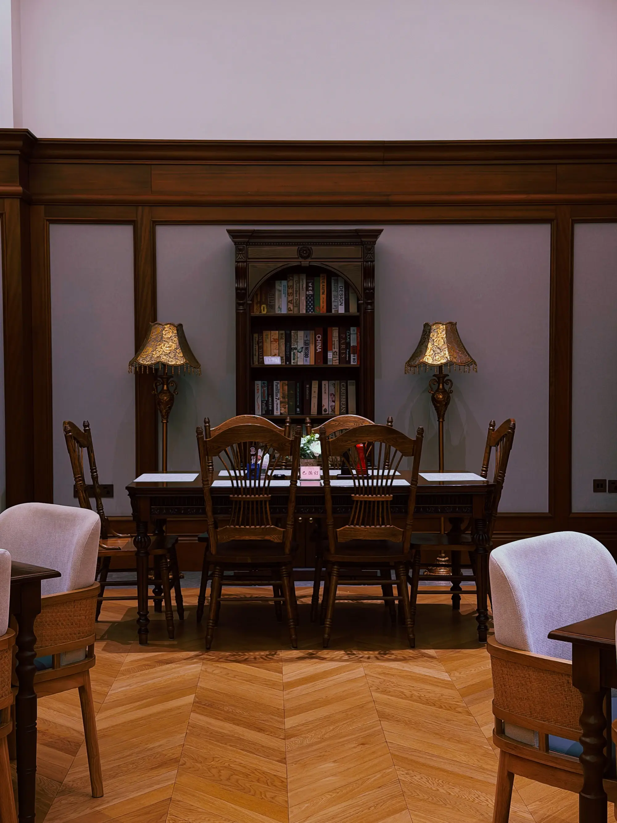 Sala riunioni con tavolo in legno, sedie imbottite, lampade da tavolo e una libreria sul fondo