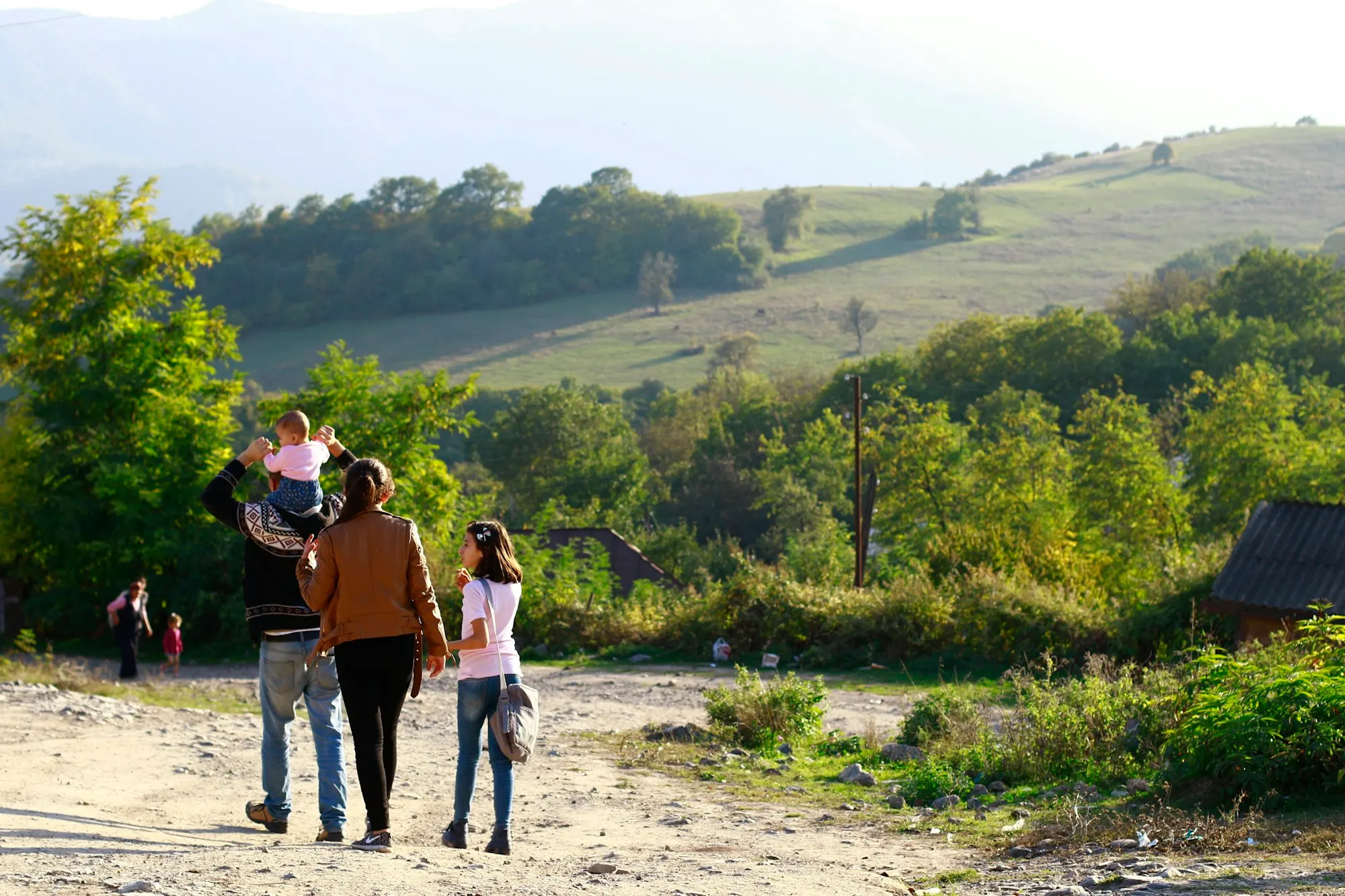 Genitori e bambini camminano insieme su un sentiero di campagna, uno dei piccoli sulle spalle del papà